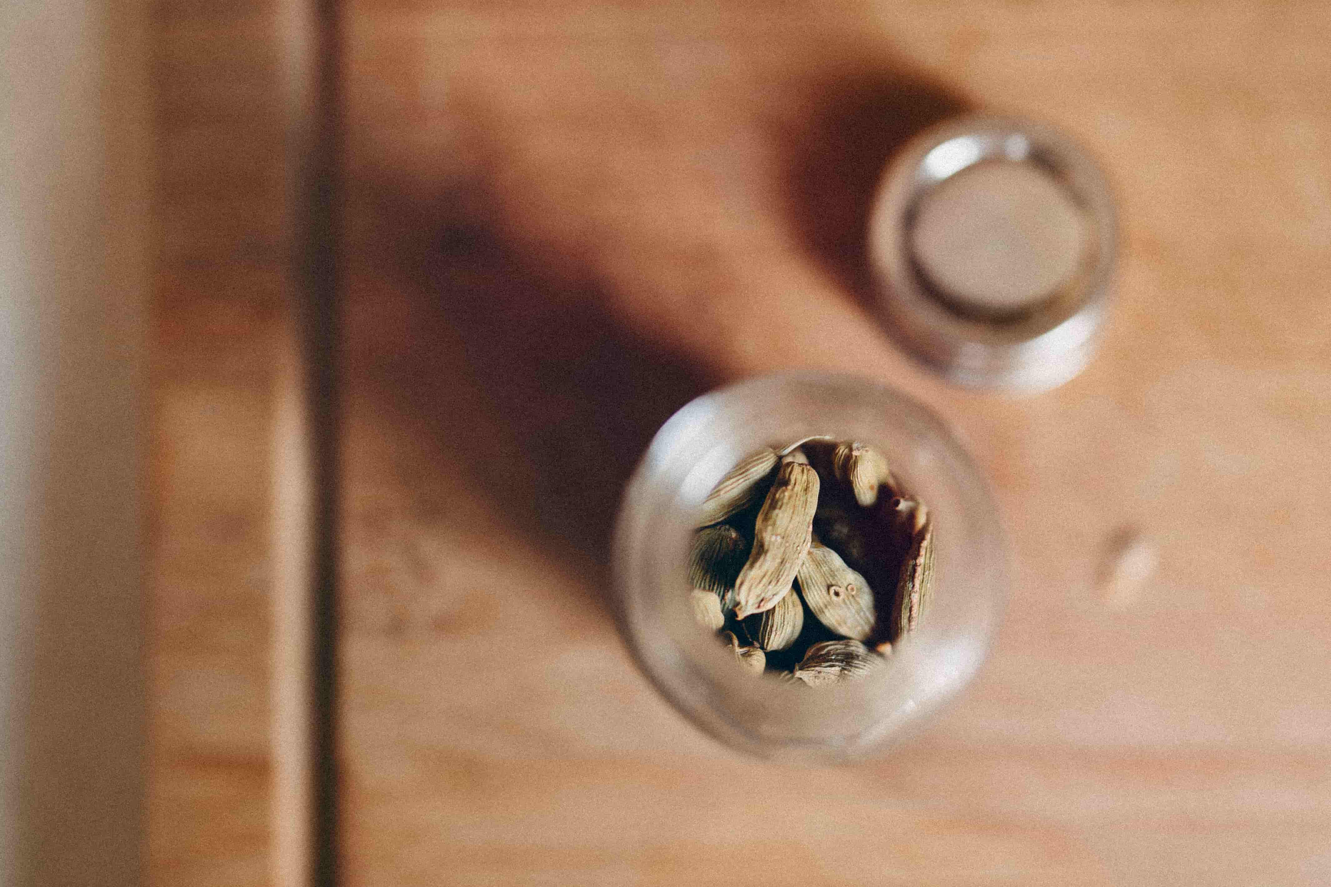 A small jar of cardamom pods on a wooden table