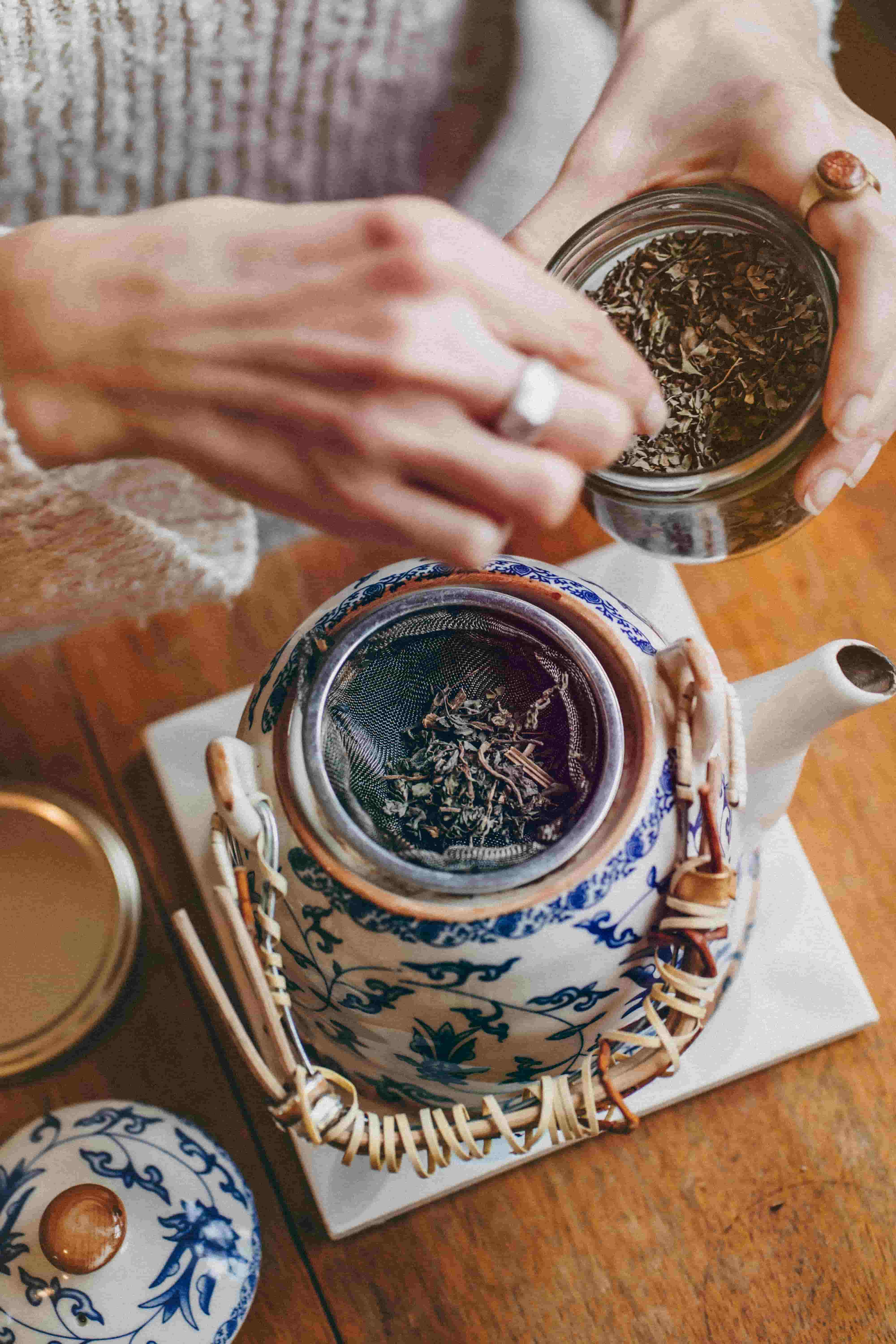 Hands preparing loose leaf tea in a teapot